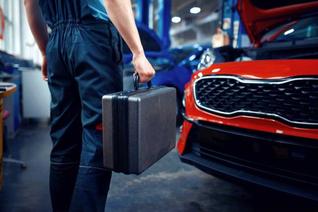 A locksmith with a toolkit stands near a red car in a garage